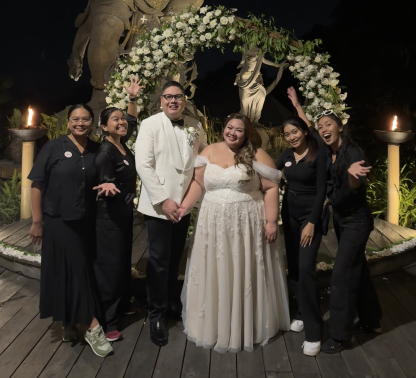 Newlyweds and The About Wedding team celebrating beneath a floral arch