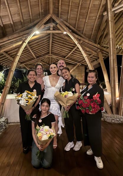 A bride posing beneath a pavilion with The About Wedding team and bouquets